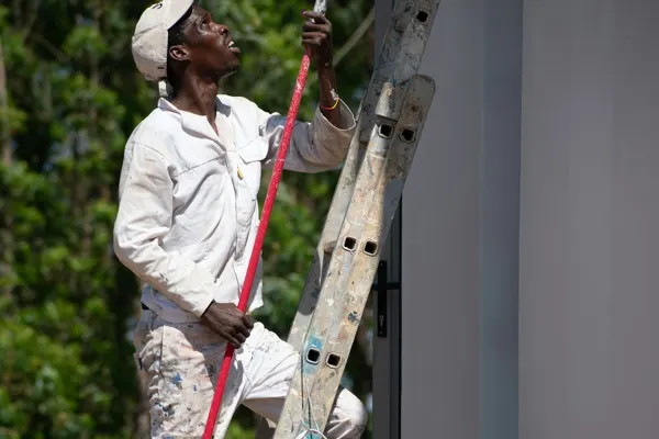 Pintor en una escalera pintando una pared exterior