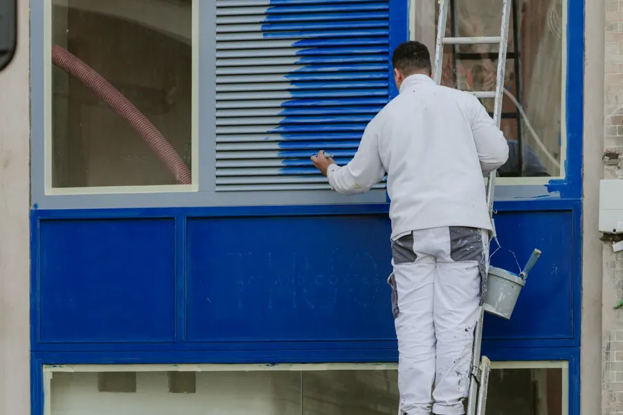 Pintor pintando una ventana de azul desde una escalera