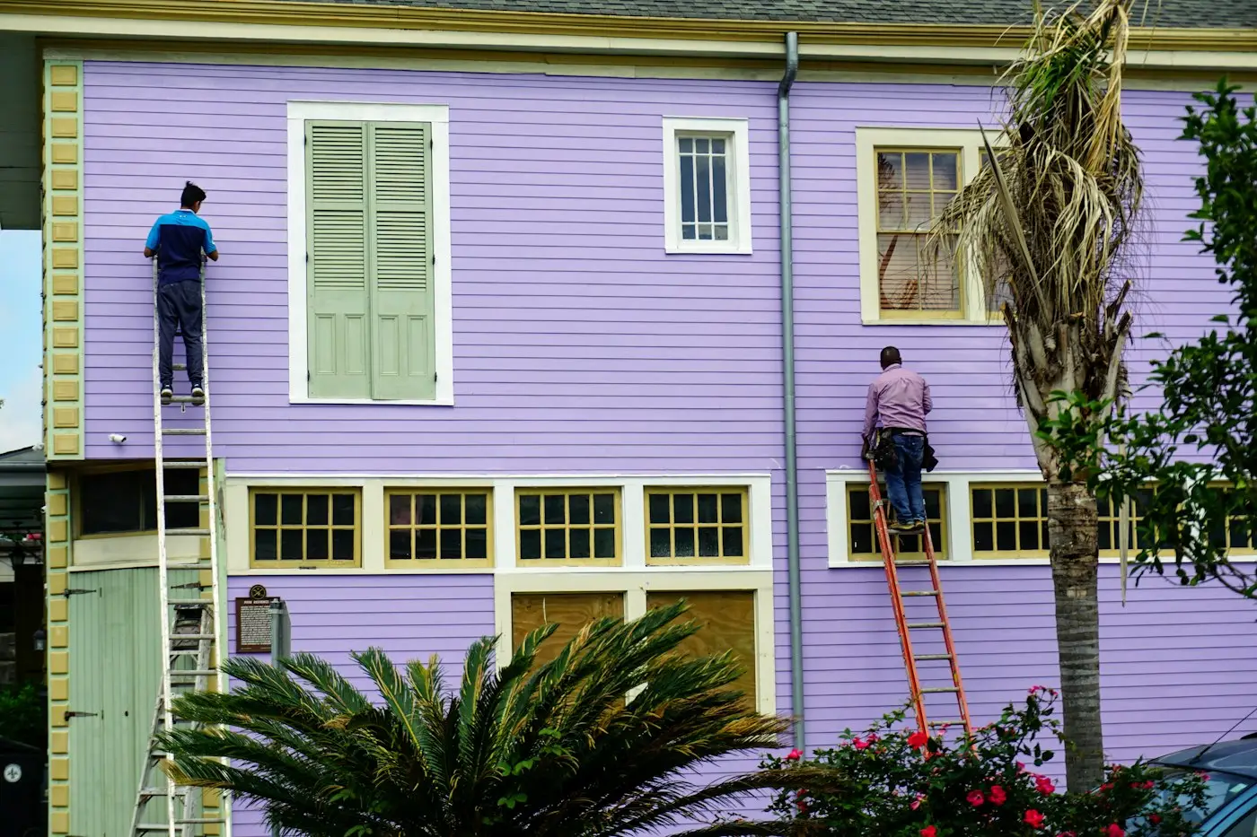 Dos pintores en escaleras pintando el frente de una casa